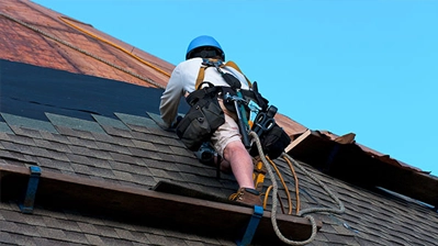 A man on a roof, wearing a harness and holding a rope, ensuring safety while working at heights.