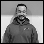 Hector, the Production Manager, wearing a hoodie, poses confidently in front of a wall.