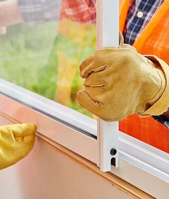 A man in gloves and an orange vest installing a new window.