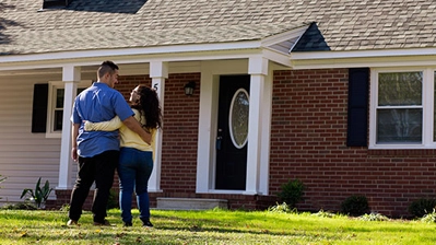 An affectionate couple posing in front of their new home.