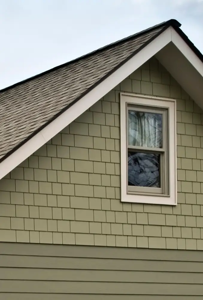 Side view of a house with a window, framed by green shingles.